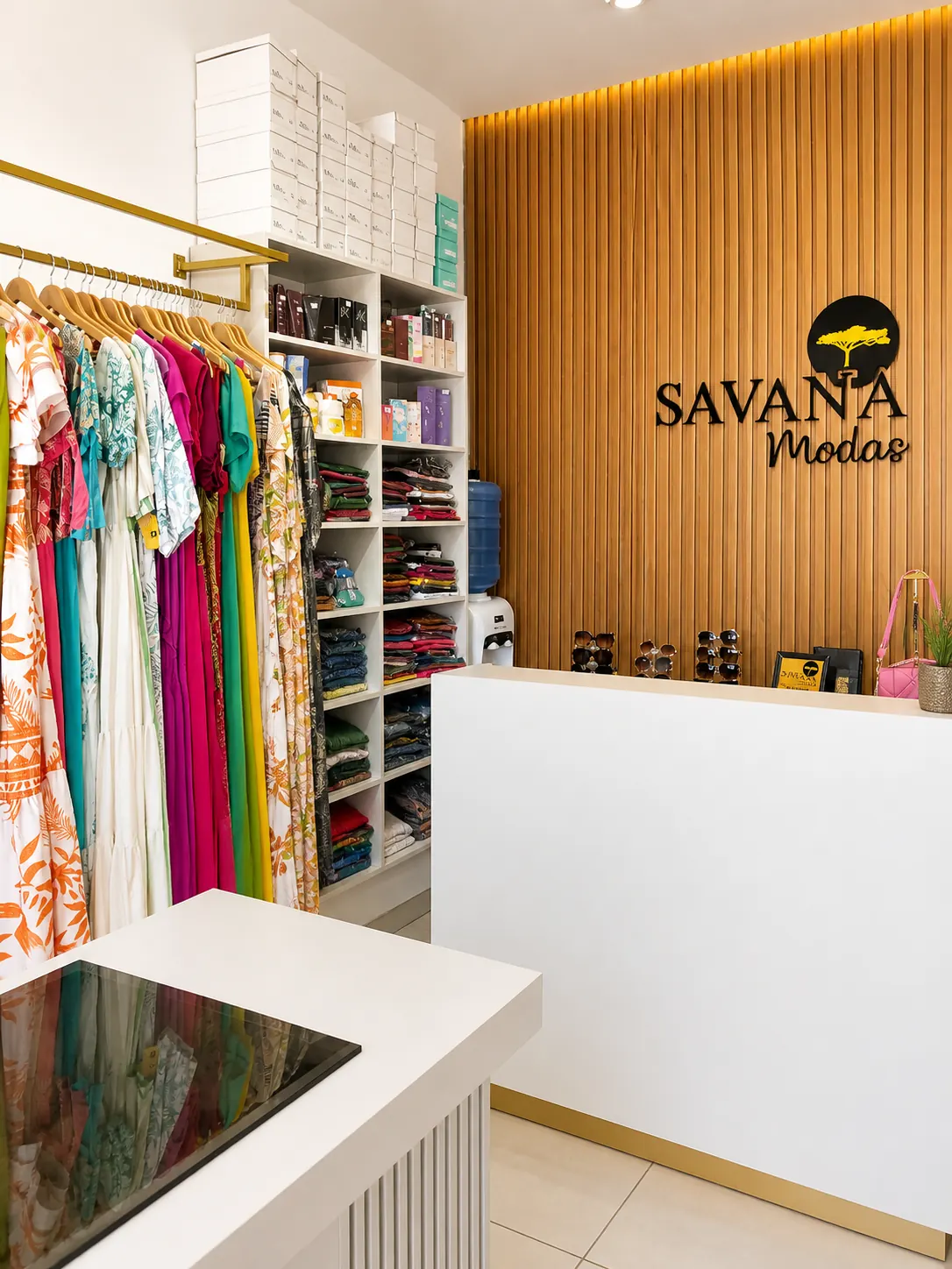 Interior da loja Savana Modas com araras de roupas coloridas e o logo na parede